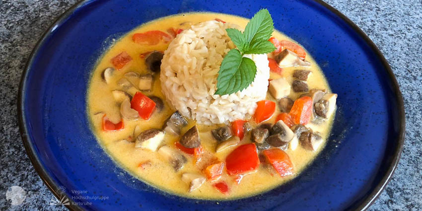 In einem blauen Teller liegt eine Reiskugel in einer Currysauce mit Champignon- und Paprikastücken.